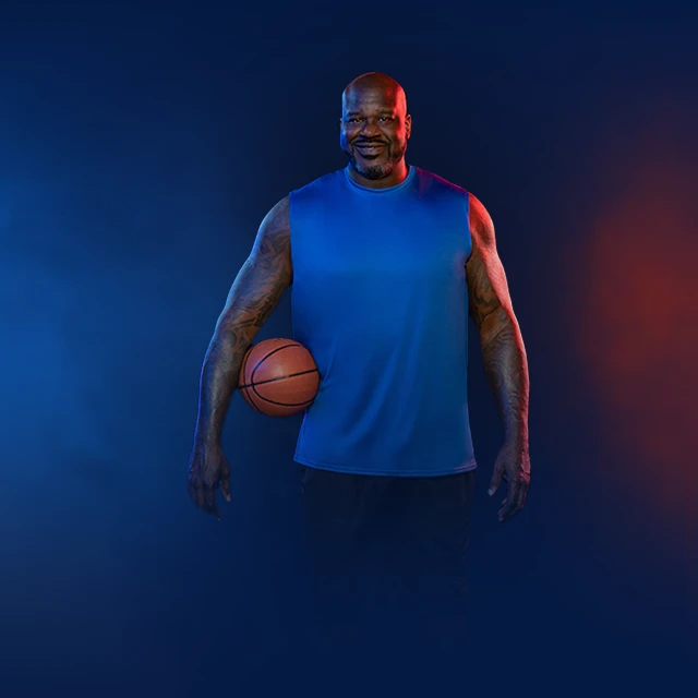 Shaquille O’Neal smiling as he holds a basket ball under his right arm.